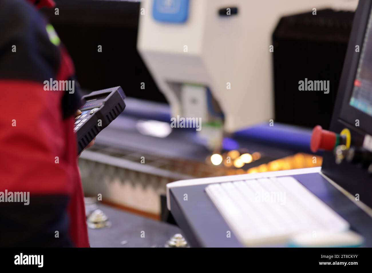 Operatore che controlla la macchina da taglio laser CNC tramite telecomando wireless. Messa a fuoco selettiva. Foto Stock