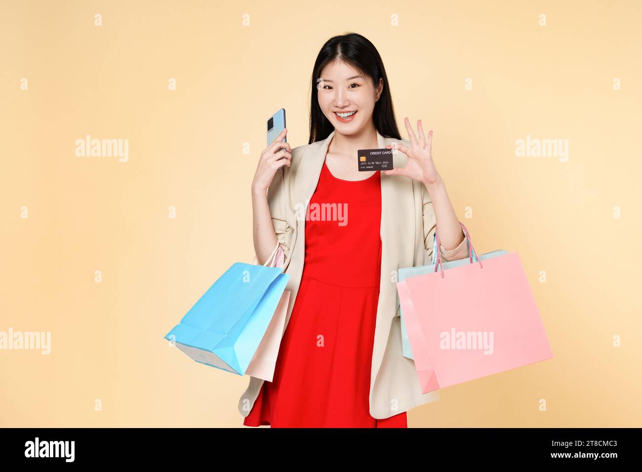 Donna asiatica che usa un telefono cellulare con carta di credito porta borse della spesa isolate su sfondo beige chiaro. Giovane ragazza sorridente che acquista online thro Foto Stock