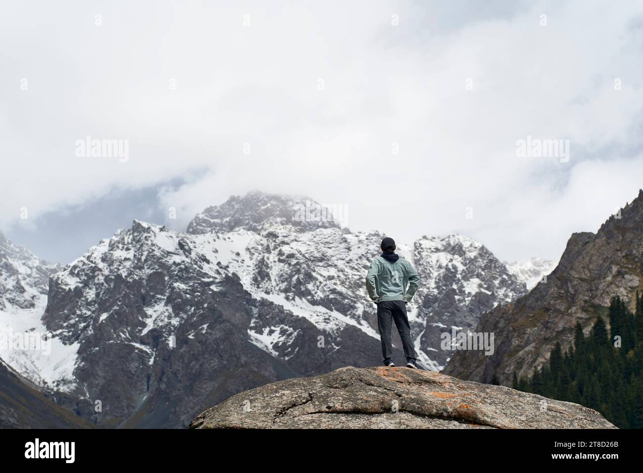 Vista posteriore di un viaggiatore asiatico in cima a una roccia che guarda una montagna di neve nello Xinjiang, Cina Foto Stock