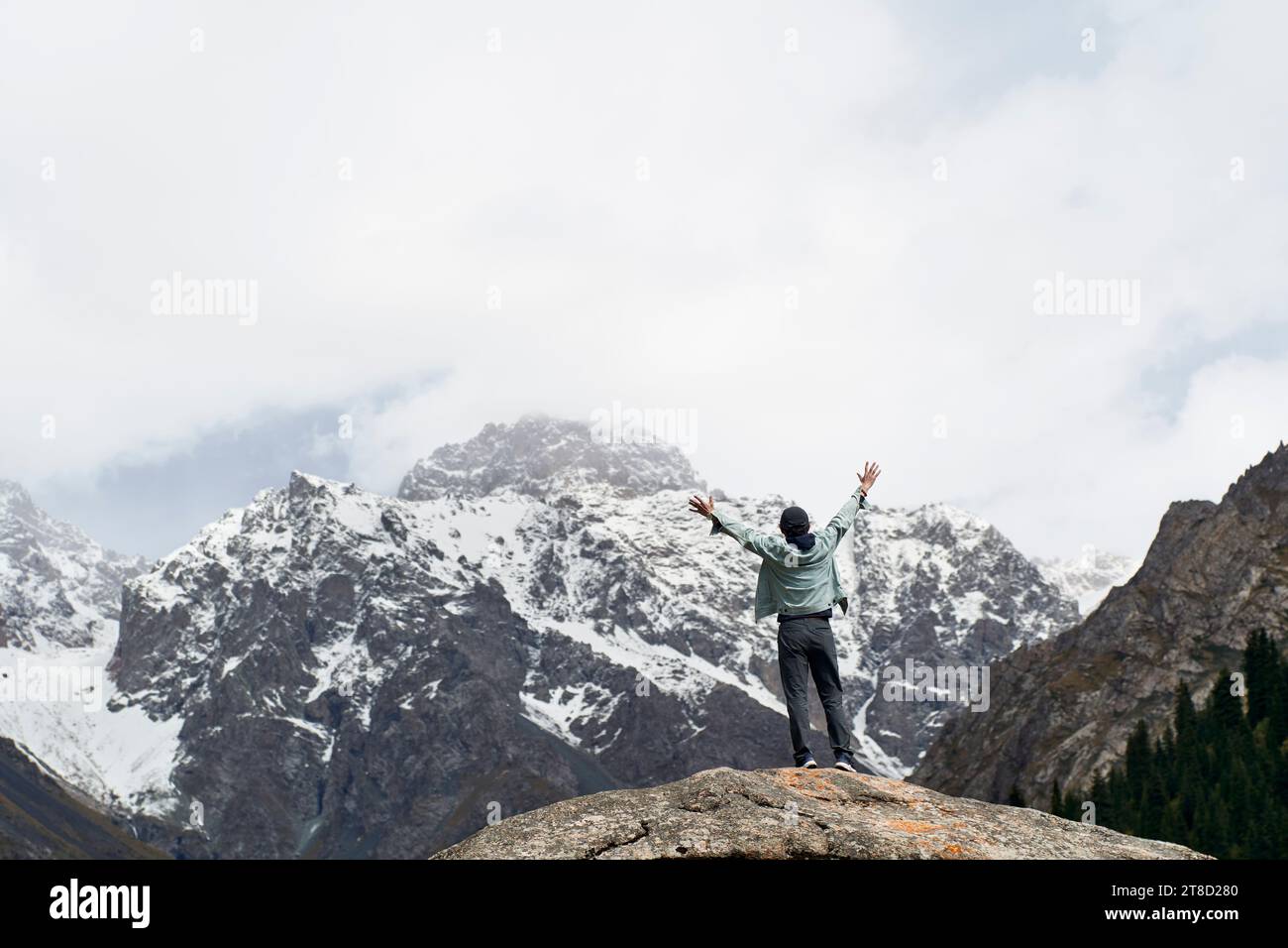 Vista posteriore di un viaggiatore asiatico in cima a una roccia che guarda una montagna di neve nello Xinjiang, Cina Foto Stock