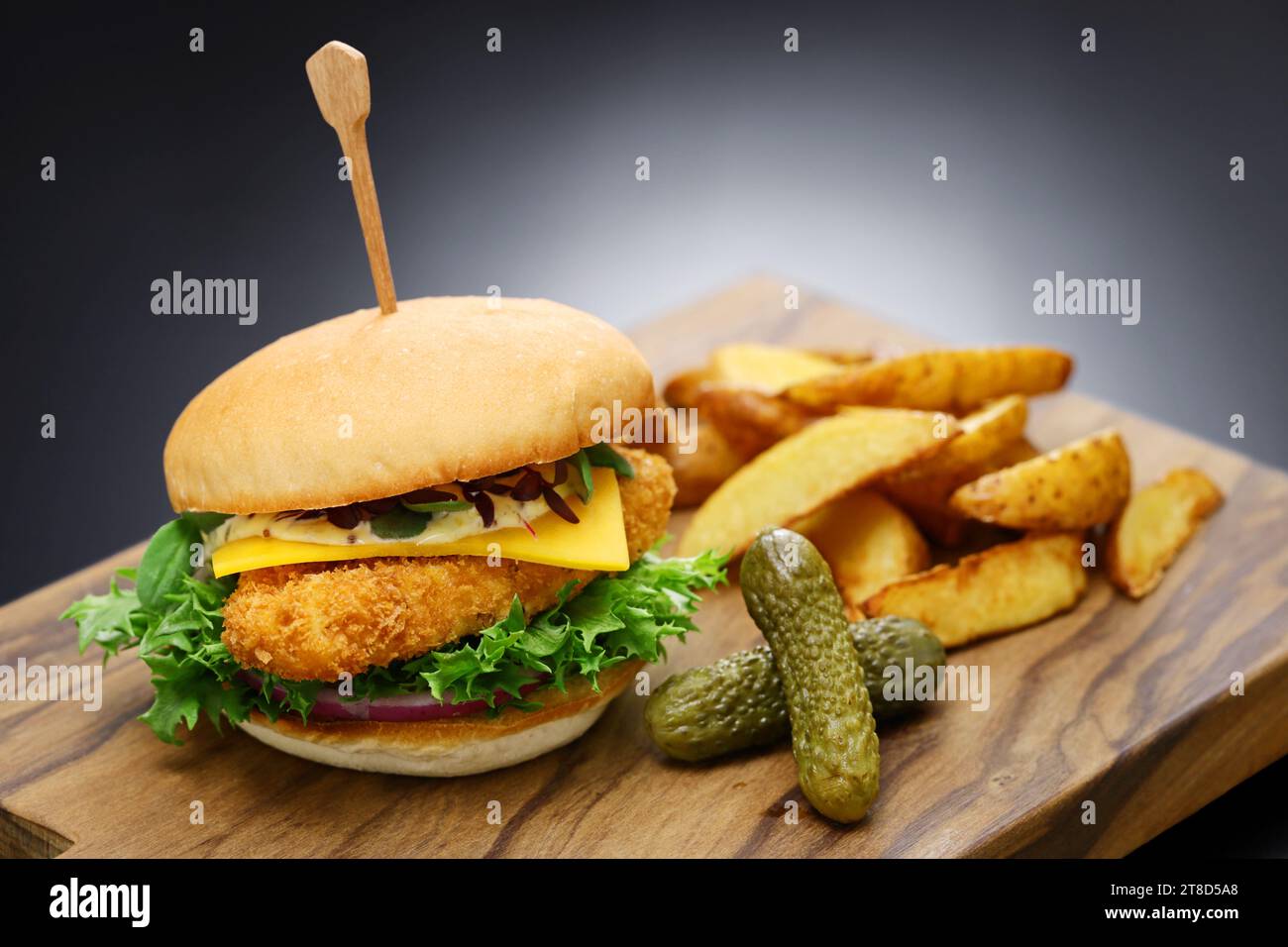 hamburger di pesce fatto in casa con formaggio, verdure e salsa tartara su un tagliere di legno. Foto Stock