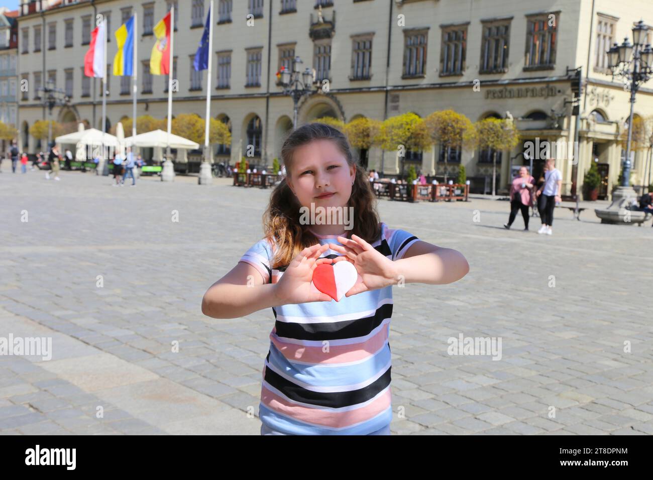 Un cuore rosso-bianco nei colori della bandiera nazionale della Polonia nelle mani di un bambino sullo sfondo della piazza della città vecchia. Giorno dell'indipendenza o Foto Stock