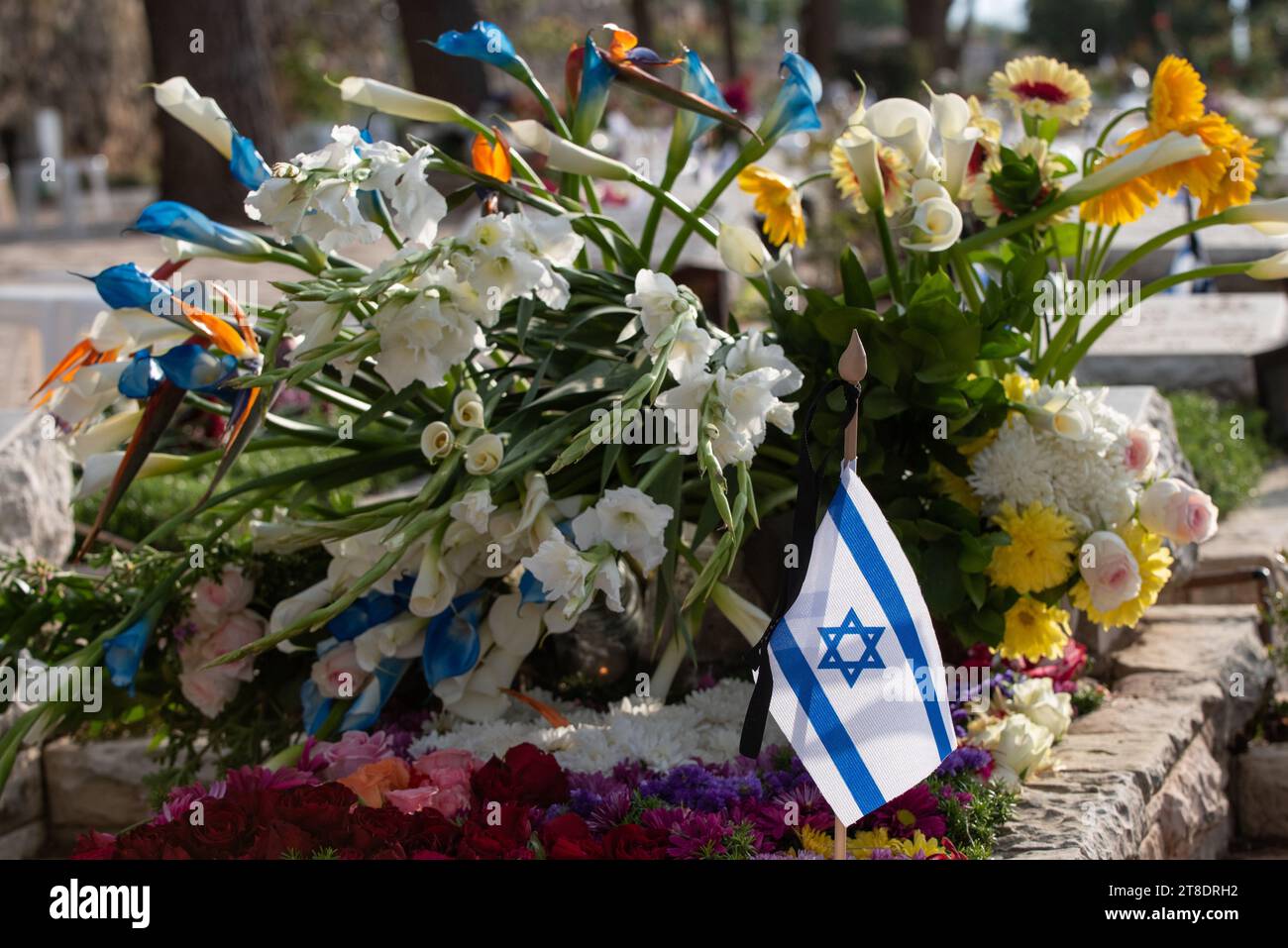 Una bandiera dello Stato di Israele poggia su una tomba di un soldato caduto coperto di fiori colorati nel cimitero militare di Har Herzl a Gerusalemme su di me Foto Stock