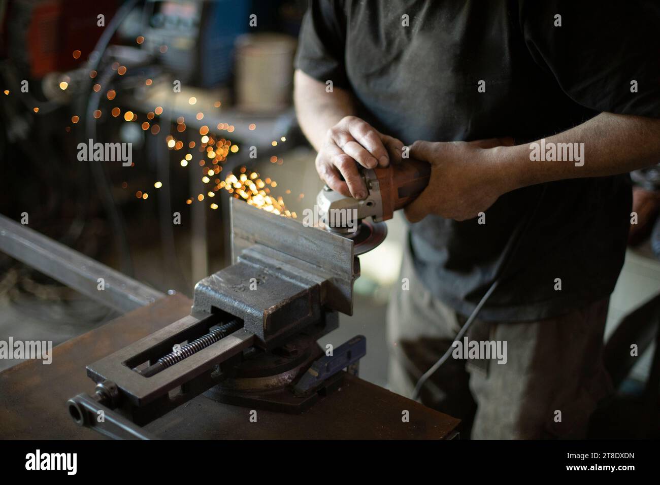 Il tizio in garage sta riparando parti in acciaio. L'uomo macina il ferro. Foto Stock