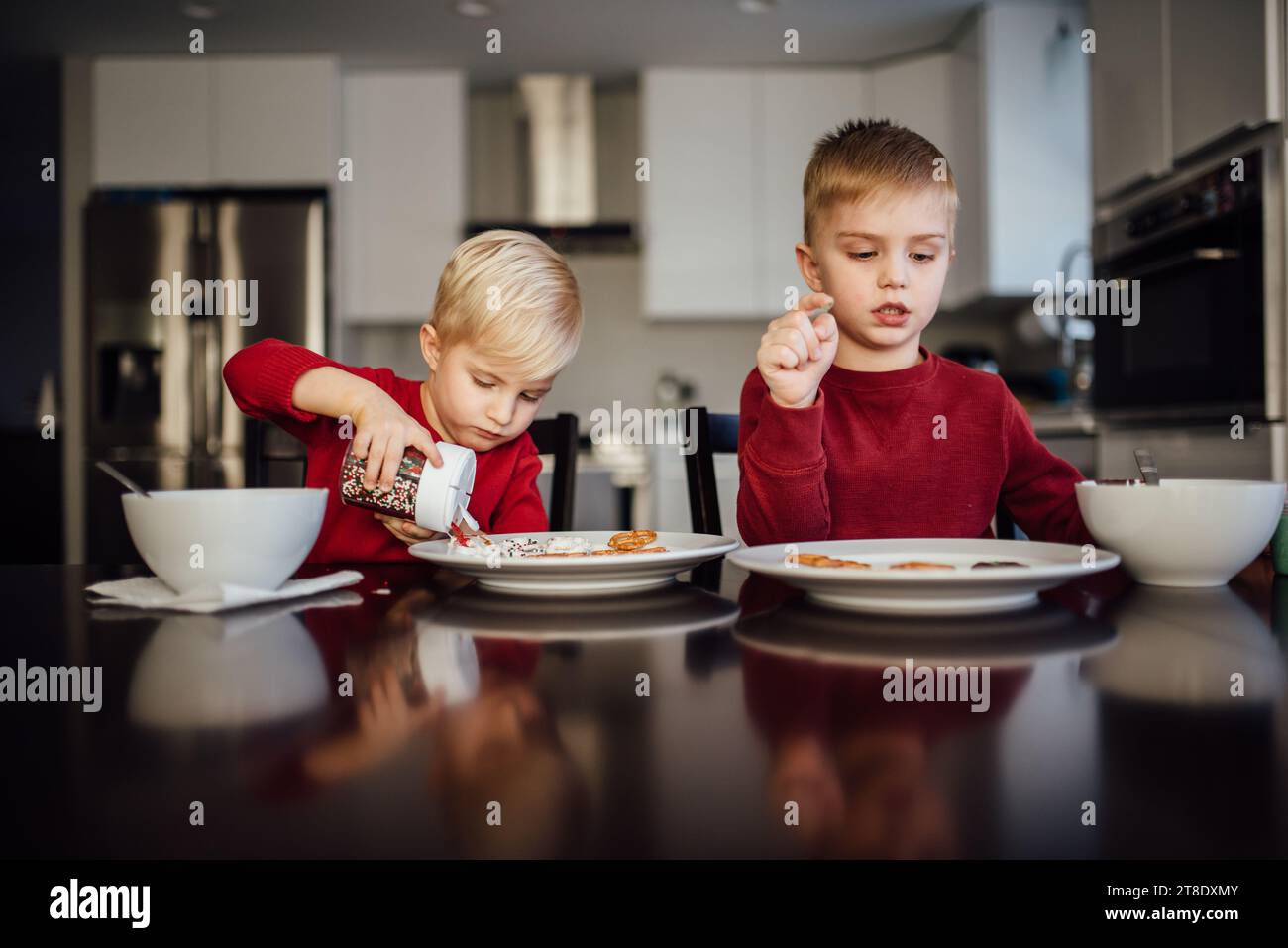 Due fratelli che indossano camicie rosse si siedono al tavolo per decorare biscotti Foto Stock