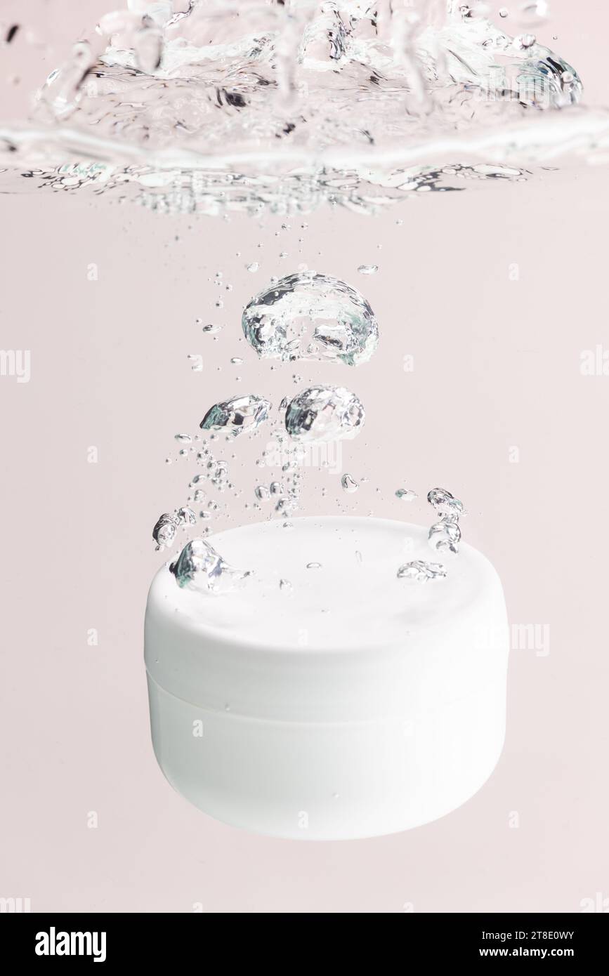 Immagine verticale della vasca del prodotto di bellezza che cade in acqua, sfondo dello spazio di copia su sfondo rosa Foto Stock
