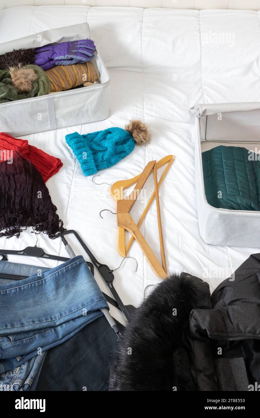 Foto orizzontale, di una stanza con vestiti invernali sdraiati sopra il letto, da raccogliere all'interno delle scatole di tessuto. Cambio armadio. Foto Stock