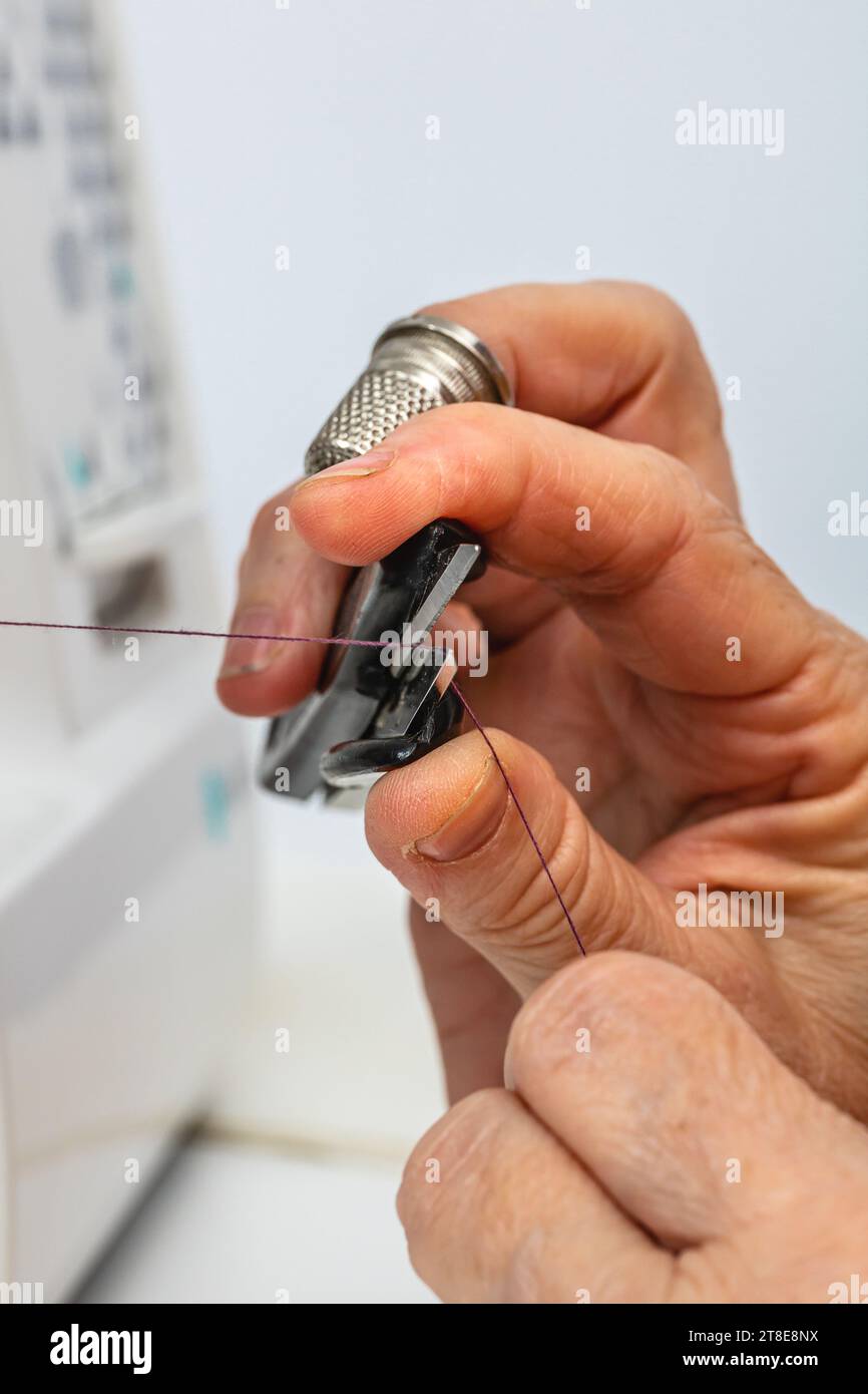 Foto verticale, mani caucasiche della sarta adulta, con ditale sul dito medio, filo da taglio con forbici sulla macchina da cucire. Foto Stock
