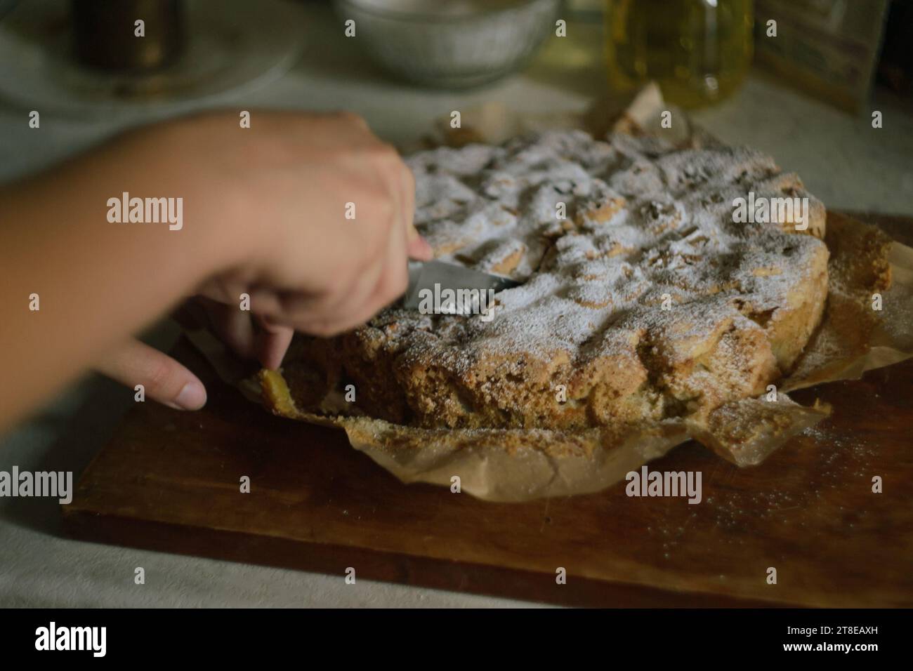 La mano di una donna taglia una torta di mele Charlotte pronta in parti uguali con un coltello in cucina su una tavola di legno Foto Stock