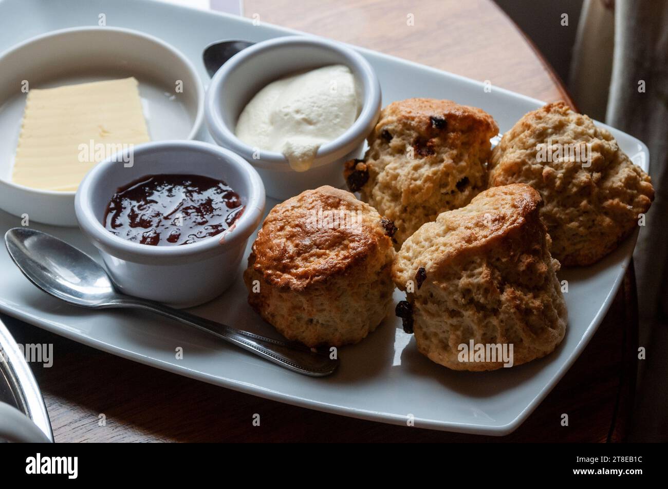 Quattro focaccine irlandesi al burro, appena sfornate, servite su un piatto con burro, marmellata e panna coagulata Foto Stock