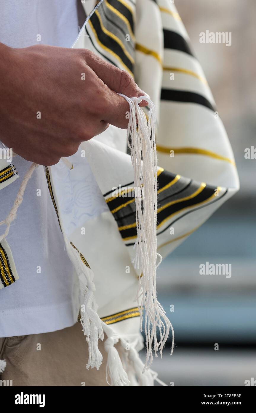 Primo piano di un uomo ebreo che prega mentre tiene le corde o lo tzitzit sul suo tallit in mano e recita lo shemà yisrael. Foto Stock