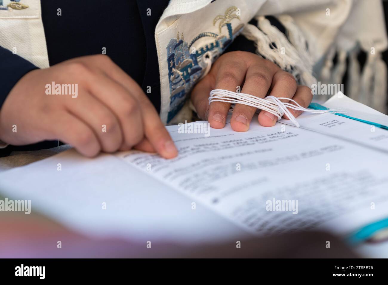 Primo piano di un uomo ebreo che prega mentre tiene le corde o tzit-tzit sul suo tallit in mano e recita lo shemà yisrael. Foto Stock