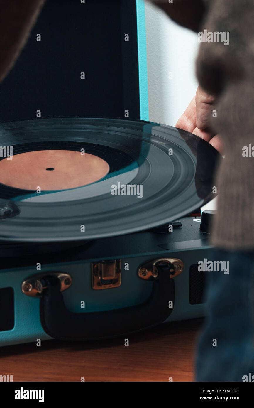 Foto ravvicinata verticale, adulto anziano maschio, caucasico, tornito alla schiena, vestito con maglione di lana marrone. Posizionamento di un vinile musicale su un lettore di dischi. stile di vita. Foto Stock