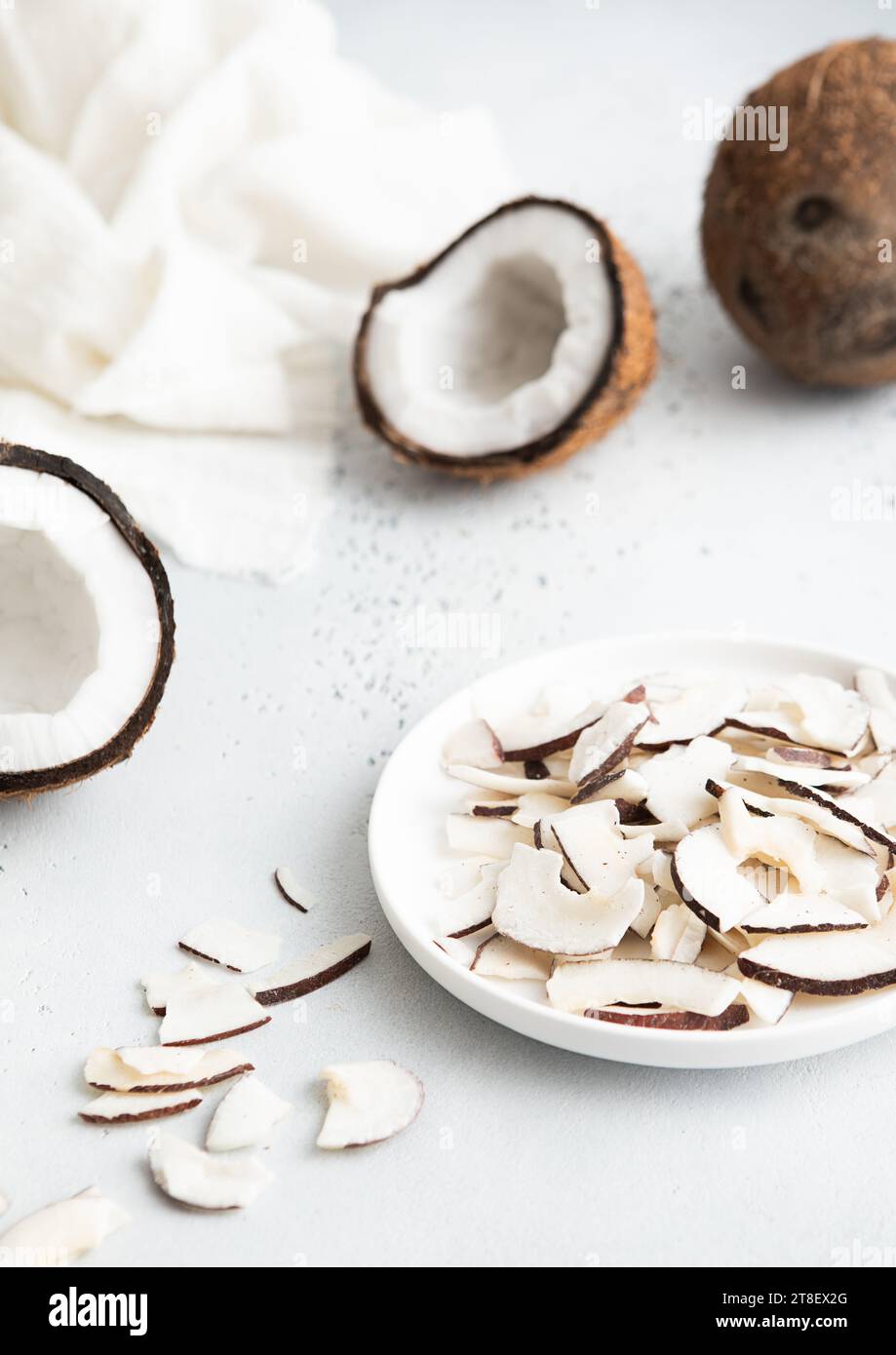 Piatto con fette di cocco organiche essiccate e cocco intero maturo su sfondo chiaro. Foto Stock