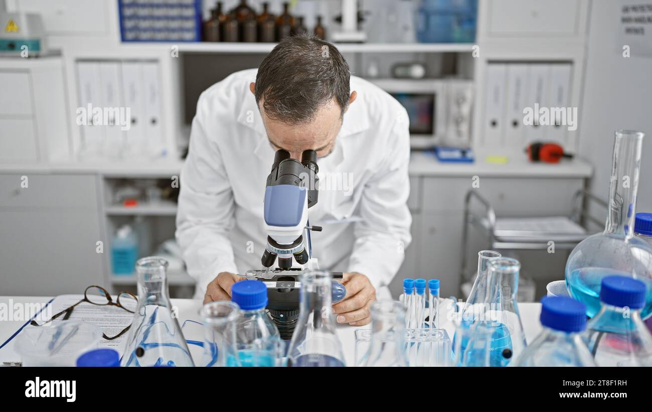 Uomo anziano con i capelli grigi, scienziato impegnato nel suo laboratorio, sfogliando nel microscopio per la scoperta medica Foto Stock