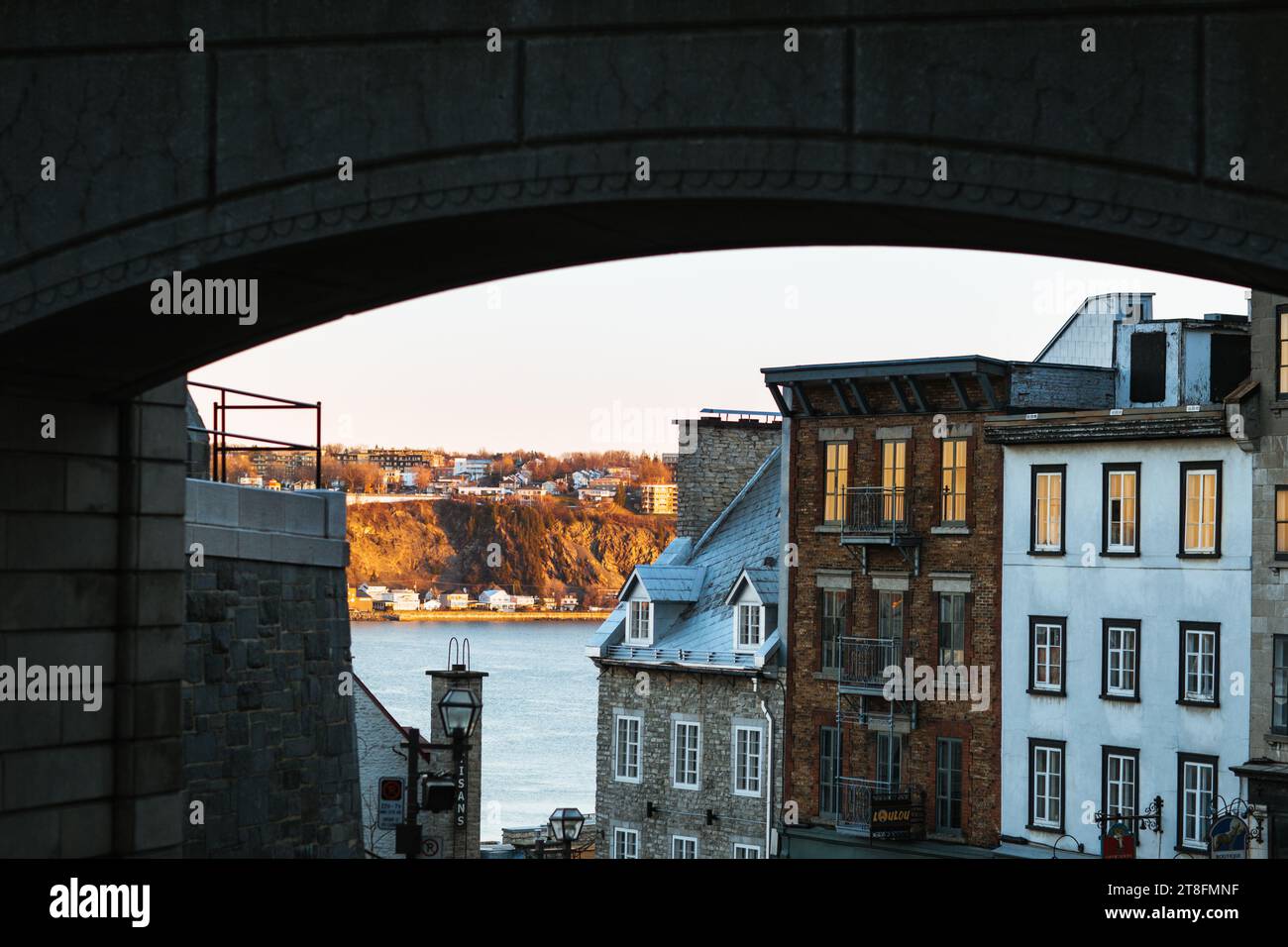 Una vista pittoresca di un paesaggio urbano con edifici storici, incorniciati da un arco, crogiolandosi nel caldo bagliore del momento dell'oro, il punto forte della luce del sole Foto Stock