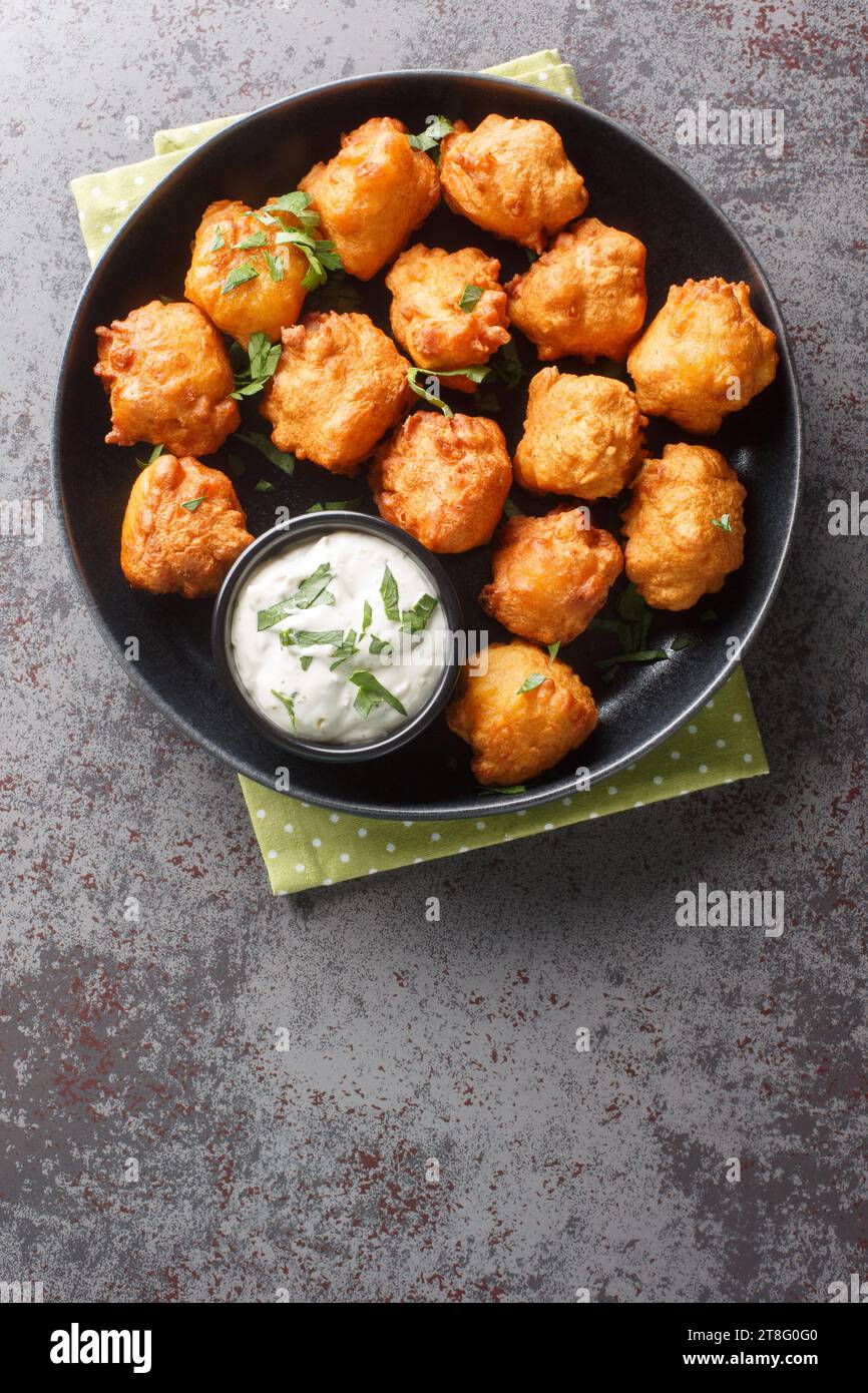 Cuccioli di spugna, cibo del sud, palle di pane di mais fritte in primo piano sul piatto sul tavolo. Vista dall'alto verticale Foto Stock
