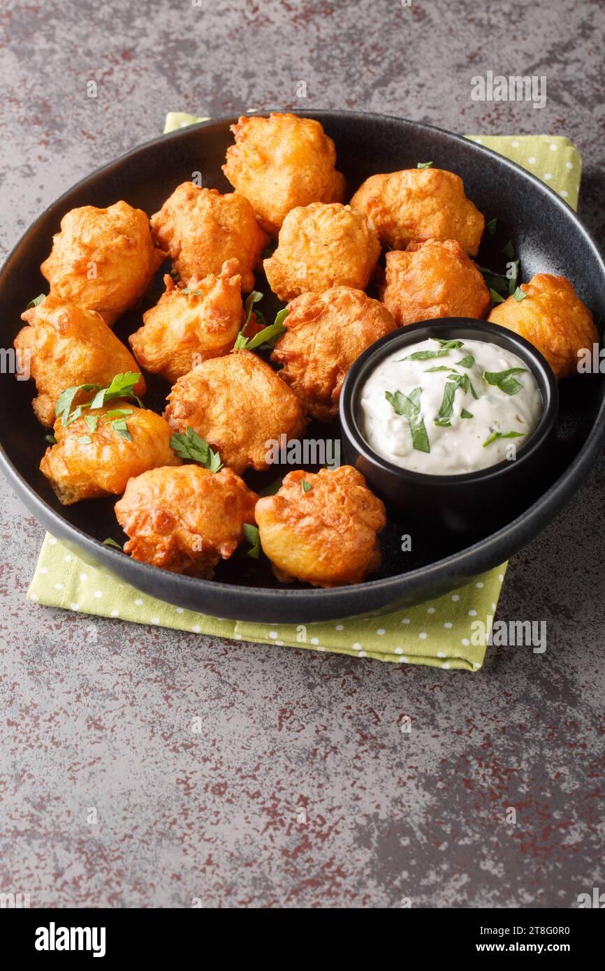 Cuccioli di spugna, cibo del sud, palle di pane di mais fritte in primo piano sul piatto sul tavolo. Verticale Foto Stock