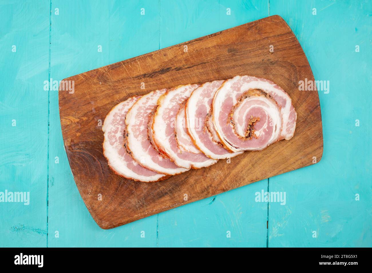 Roulade di carne di maiale tagliata su un tagliere di legno, distesa su fondo blu Foto Stock