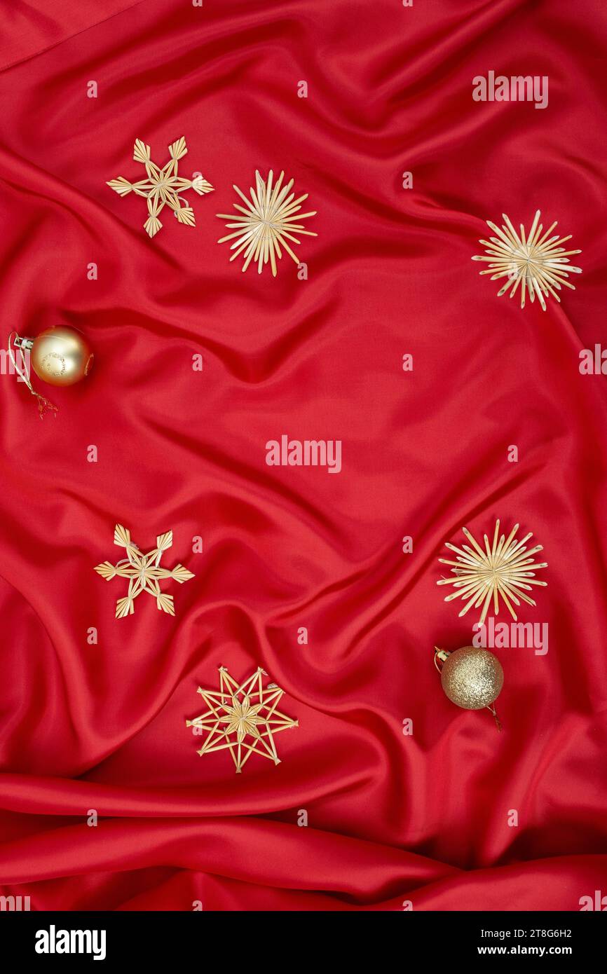 Sfondo in raso rosso con fiocchi di paglia e bauble dorati, sfondo natalizio o Capodanno Foto Stock