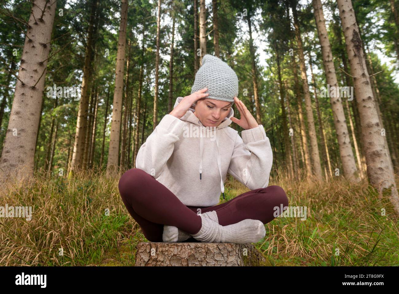 donna seduta in una foresta con la testa nelle mani, liberandosi di emozioni negative Foto Stock