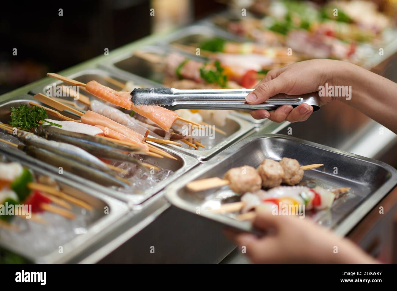 Mani di persona che prende vari spiedini dalla stalla del mercato Foto Stock