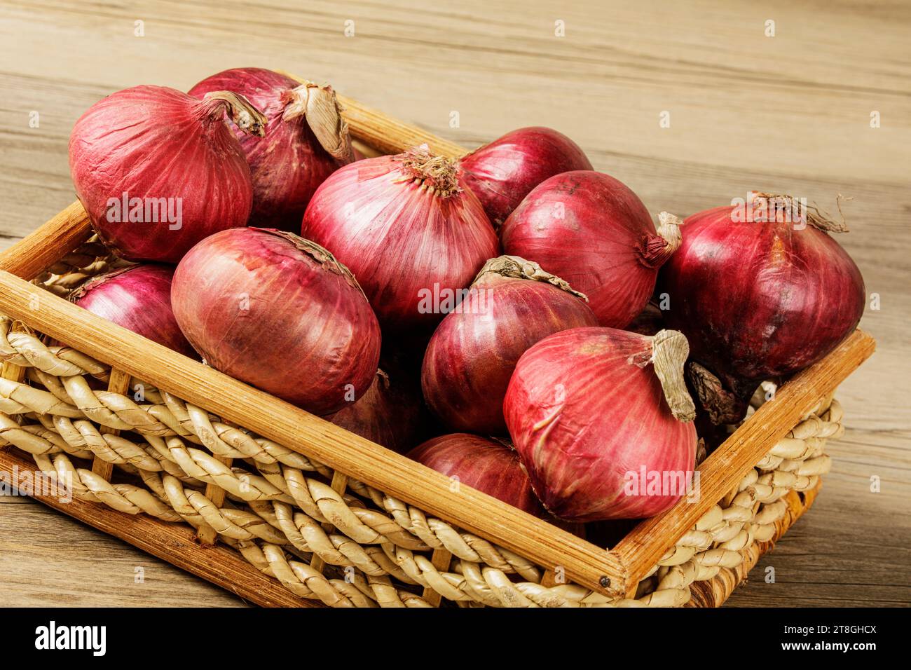 Primo piano di un cestino di cipolle rosse su uno sfondo di legno con spazio per la copia Foto Stock