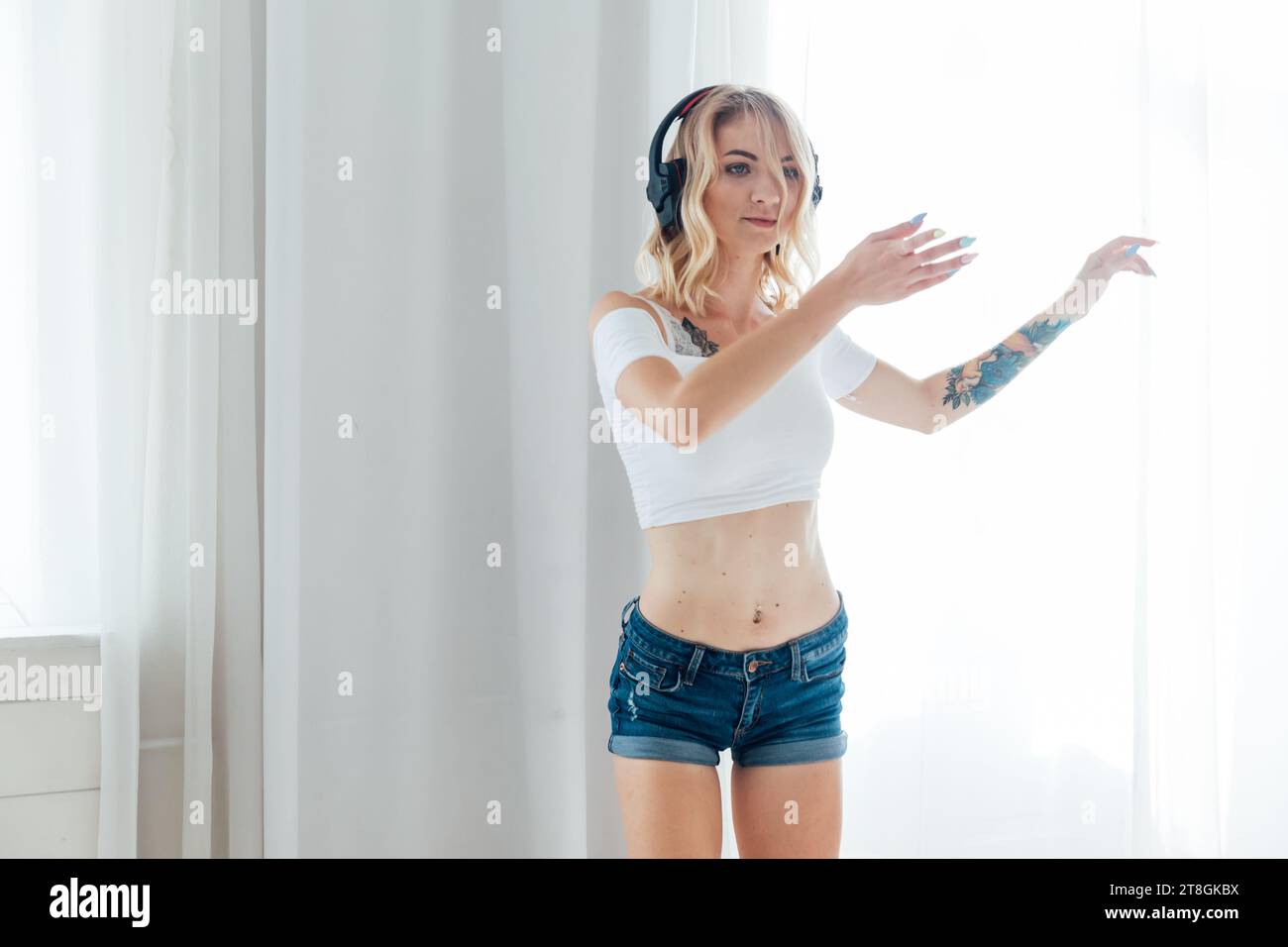 una donna con le cuffie ascolta musica e balla in una stanza luminosa Foto Stock