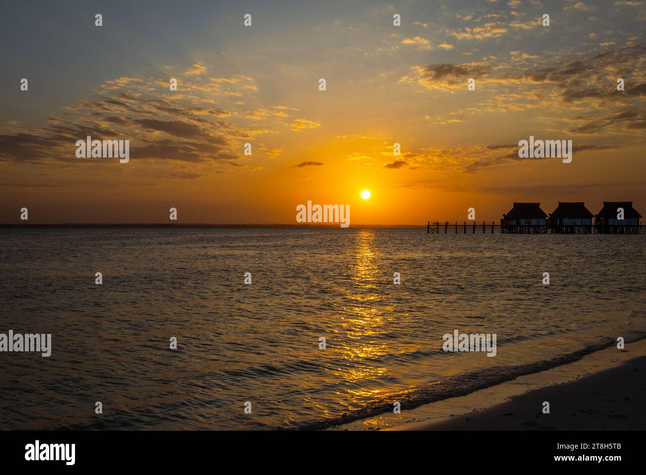 Foto orizzontale del tramonto che si riflette nel mare con molo e capanne a Zanzibar, Tanzania Foto Stock