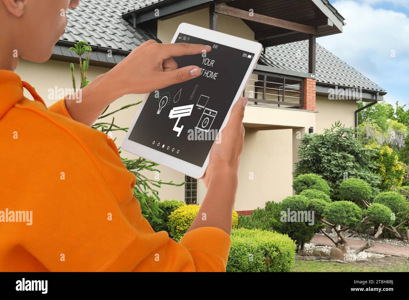 Uomo che utilizza un sistema di controllo intelligente per la casa tramite tablet vicino a casa all'aperto, primo piano Foto Stock
