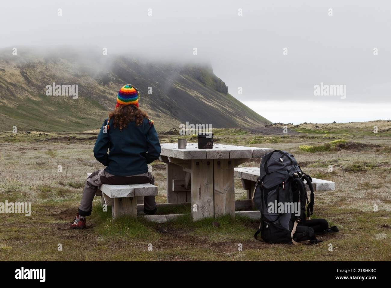 Snaefellsness/Islanda - 22 luglio 2016: Giovane donna in riposo in Islanda. Tavolo in legno con panchine e grande zaino di viaggiatori. Picnic a Icela Foto Stock