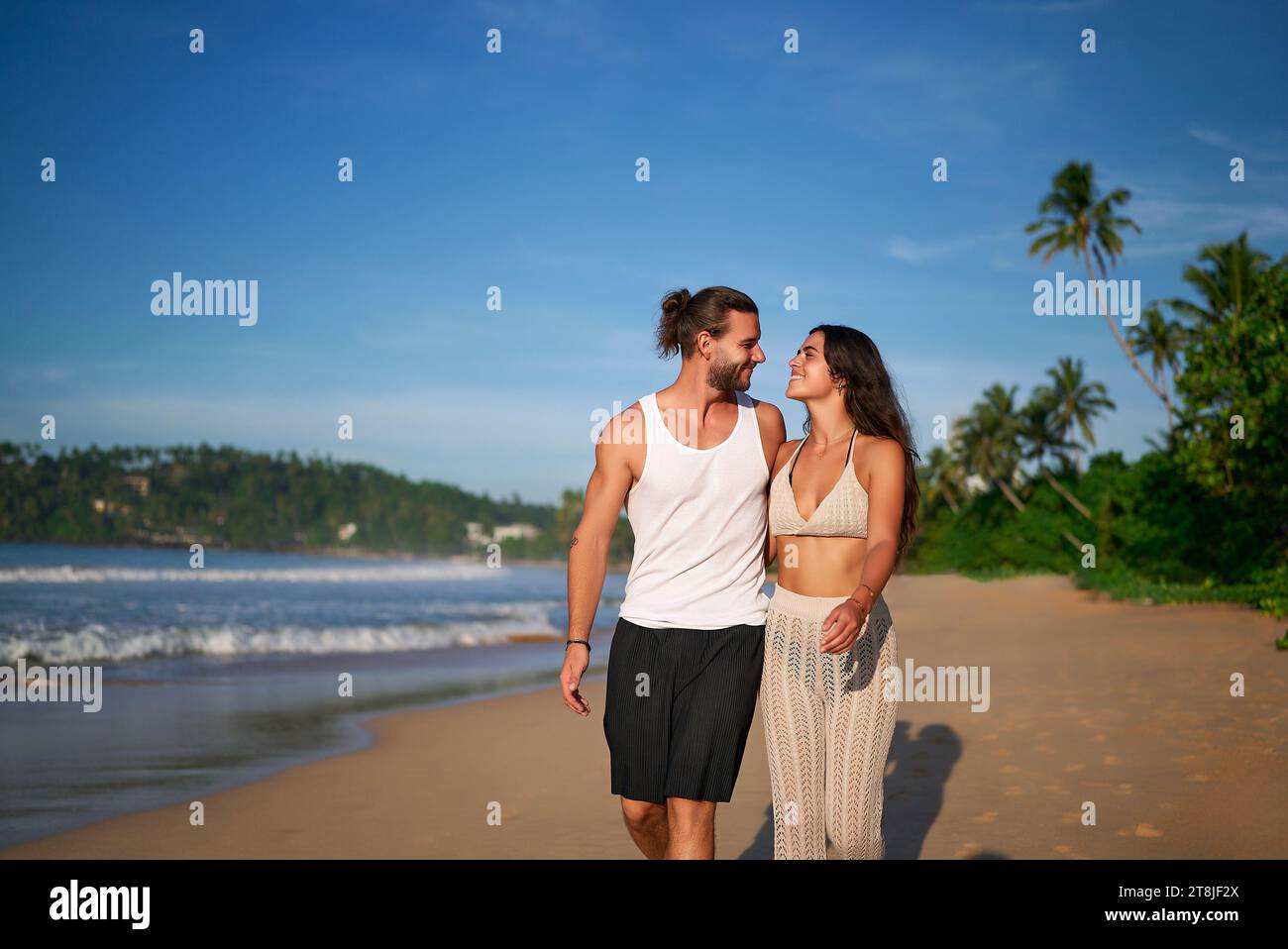 Romantiche passeggiate di coppia sulla spiaggia al tramonto, uomo a piedi nudi, donna in abiti estivi informali divertiti a passeggiare sul mare. Coppia amorevole in vacanza, in viaggio di piacere Foto Stock