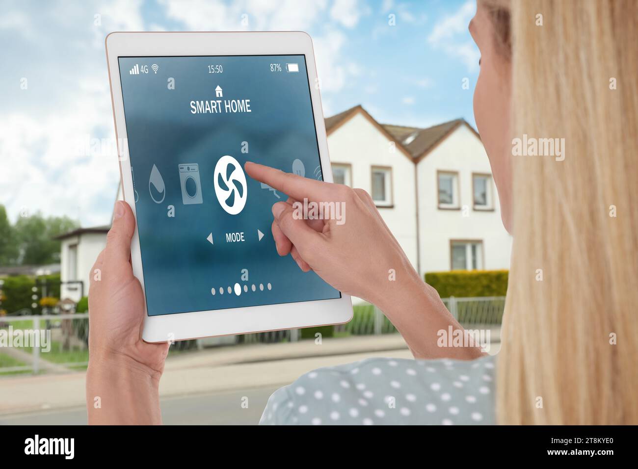 Donna che utilizza un sistema di controllo domestico intelligente tramite tablet vicino a casa all'aperto, primo piano Foto Stock
