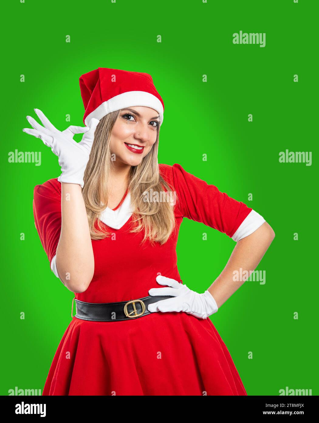 La giovane babbo natale fa un gesto discreto con la mano sorridente guardando la fotocamera su sfondo verde. concetto di natale Foto Stock