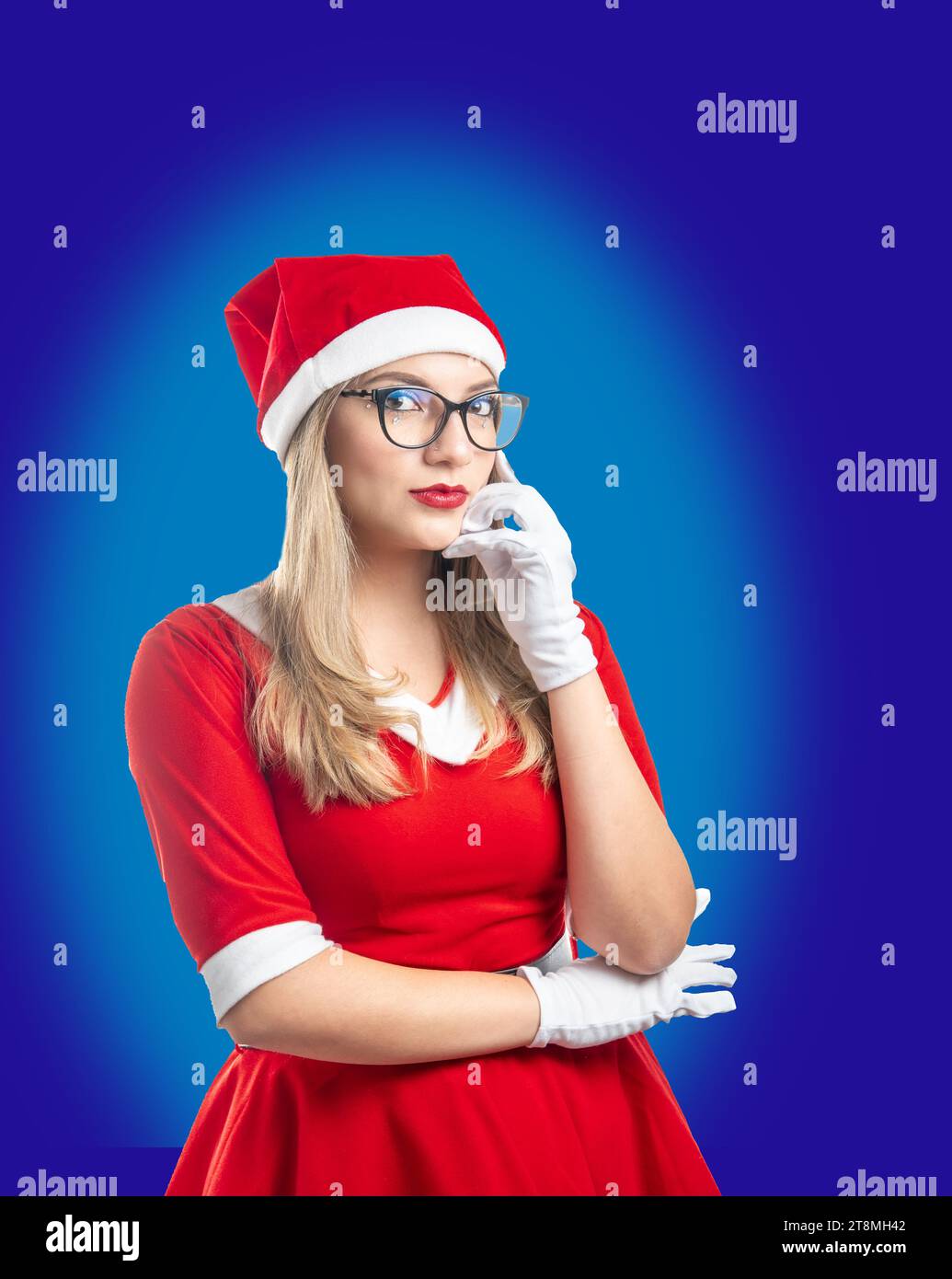 Giovane bionda Babbo Natale con gli occhiali che guardano con cura la fotocamera su sfondo blu Foto Stock