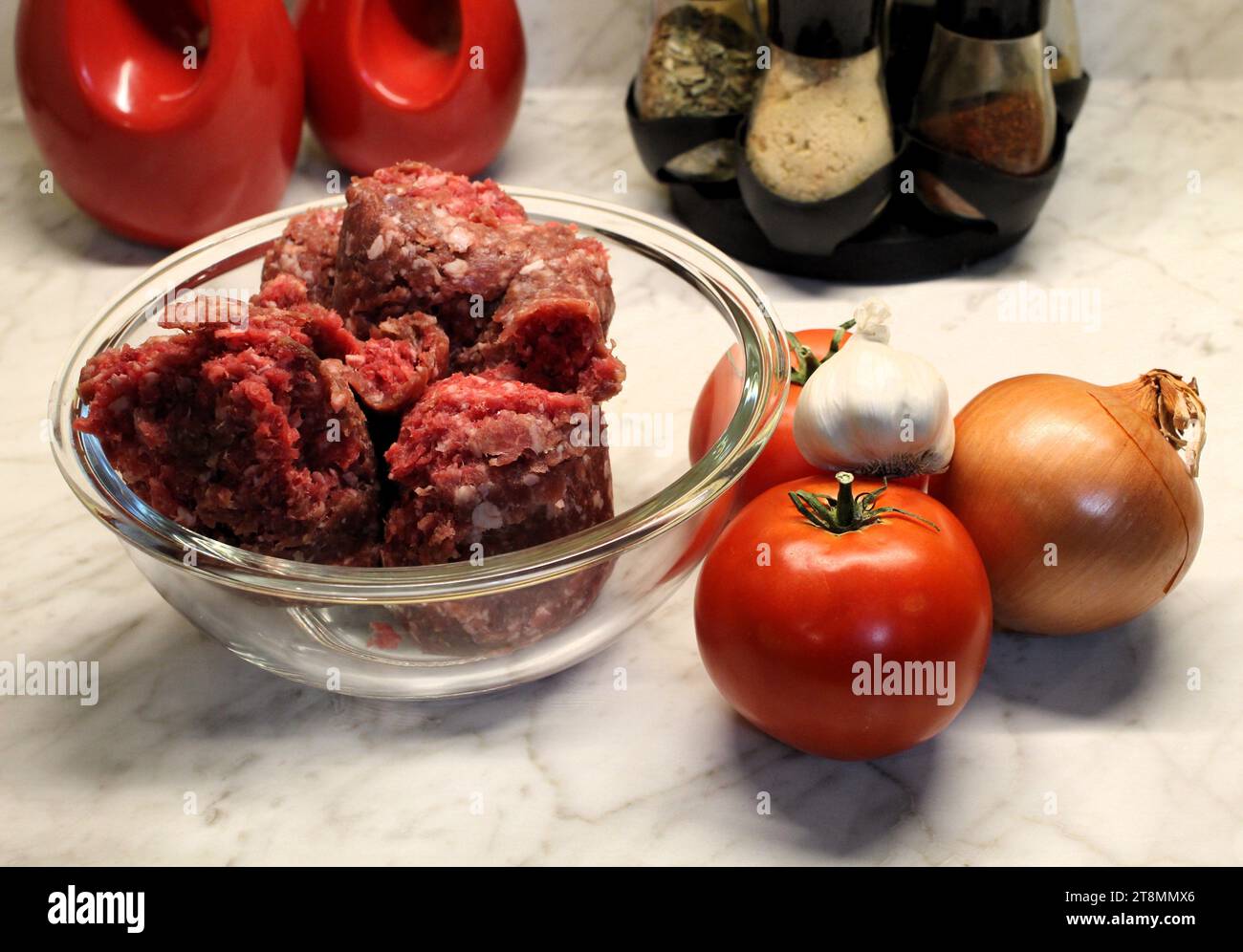 manzo macinato fresco in una ciotola di vetro con verdure e ingredienti da cucina sullo sfondo sul bancone della cucina Foto Stock
