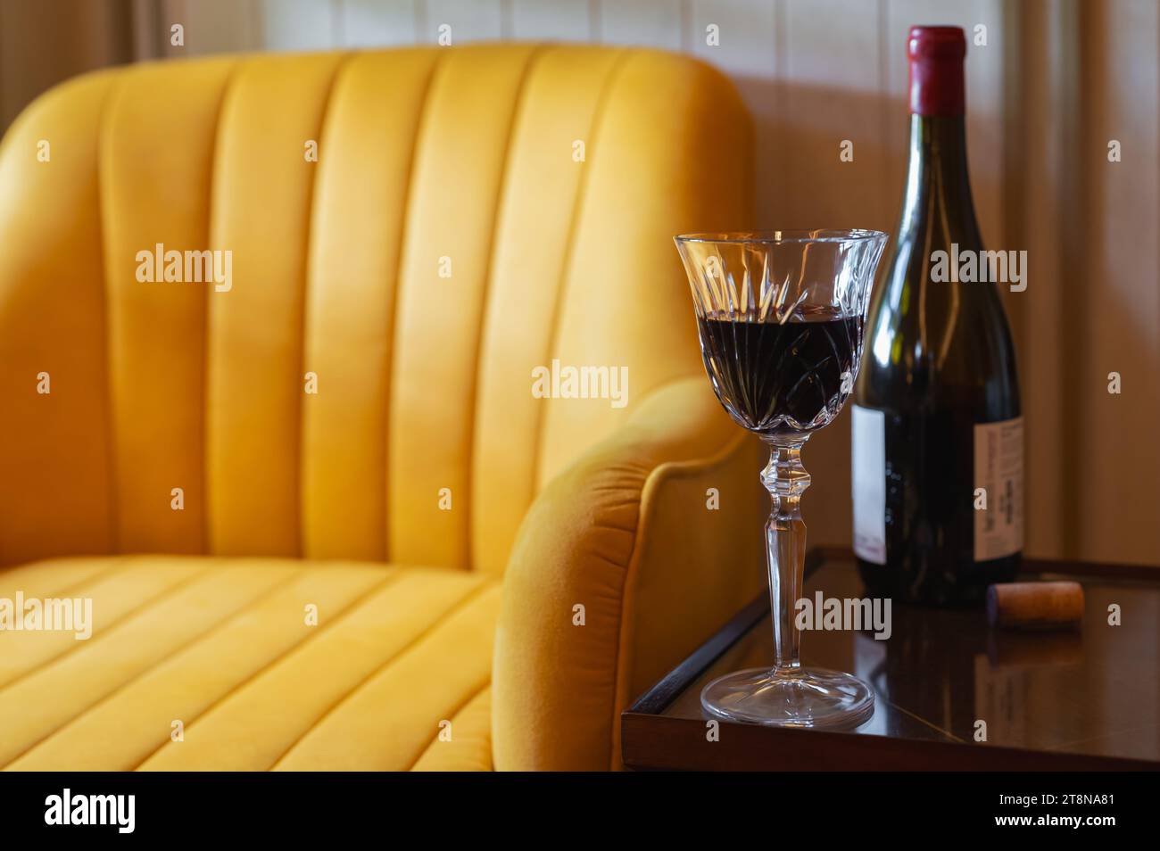 Un bicchiere di vino rosso con una bottiglia sul tavolo accanto al divano della casa per godersi un momento di relax. Foto Stock