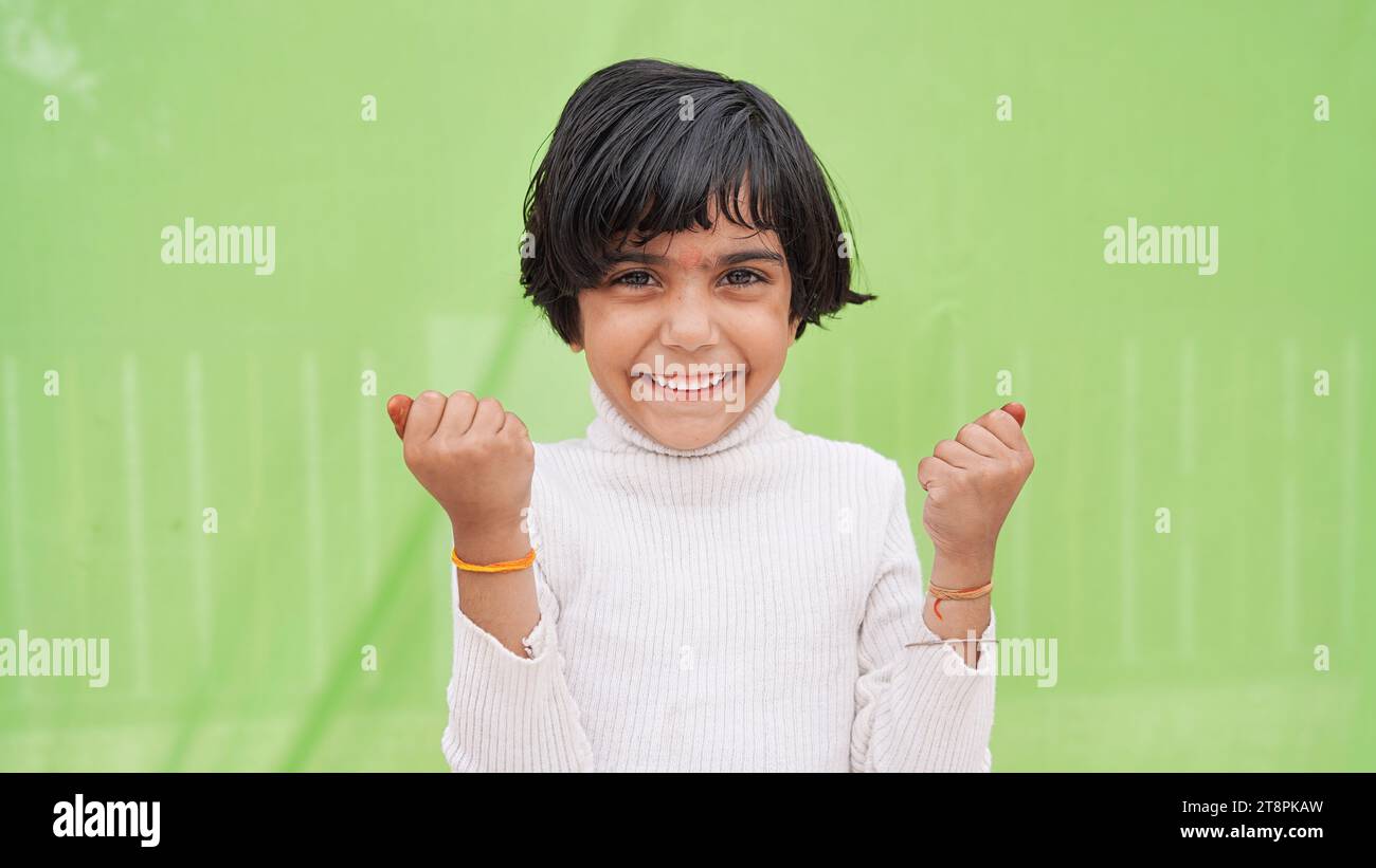 Concetto Win. Ritratto di un bambino asiatico eccitato con le mani alzate che scuotono i pugni su sfondo verde Foto Stock