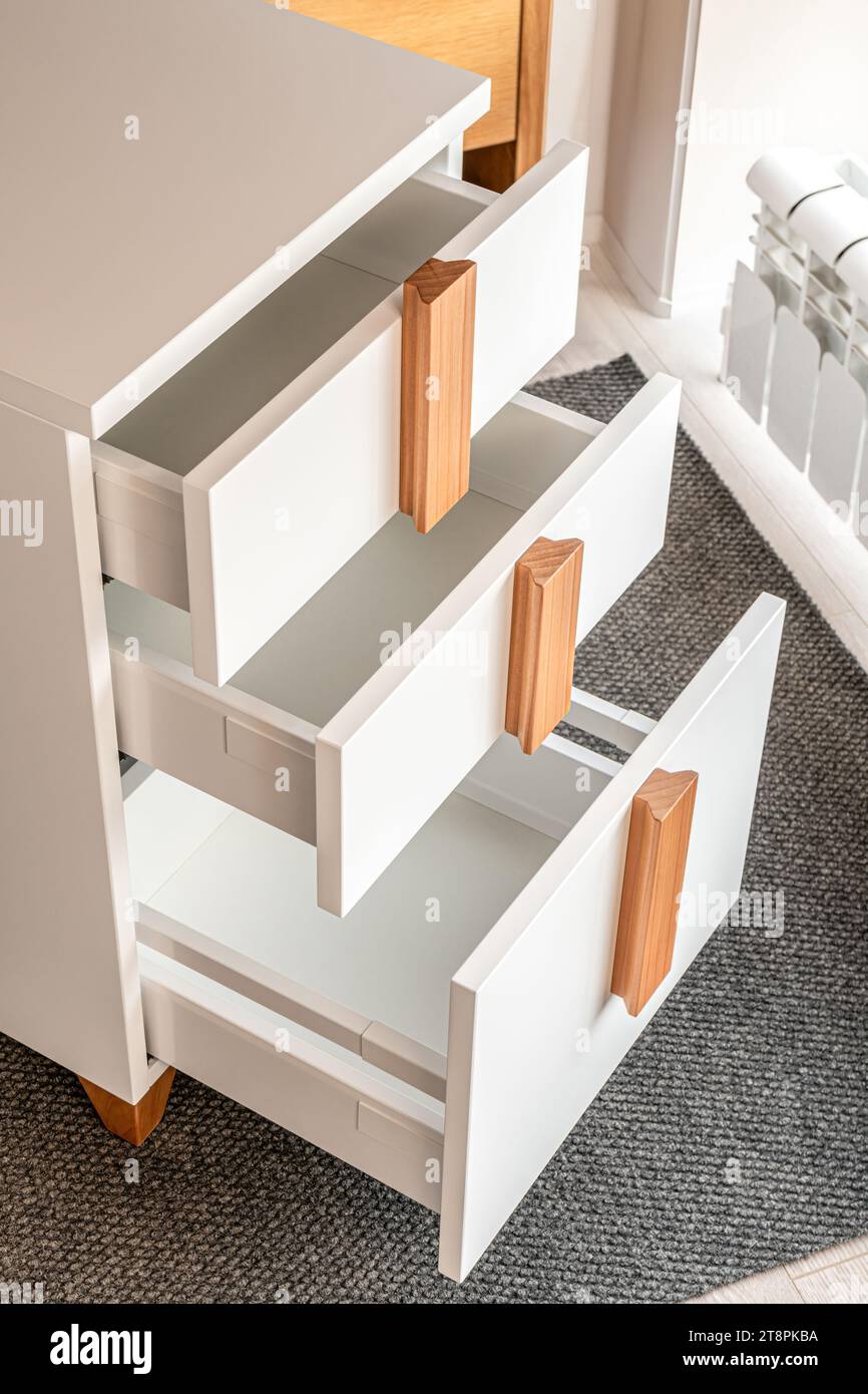 Elegante comò bianco per ufficio con maniglie e gambe in legno con cassetti aperti e vuoti, vista ravvicinata. Arredi confortevoli per la casa e l'ufficio Foto Stock