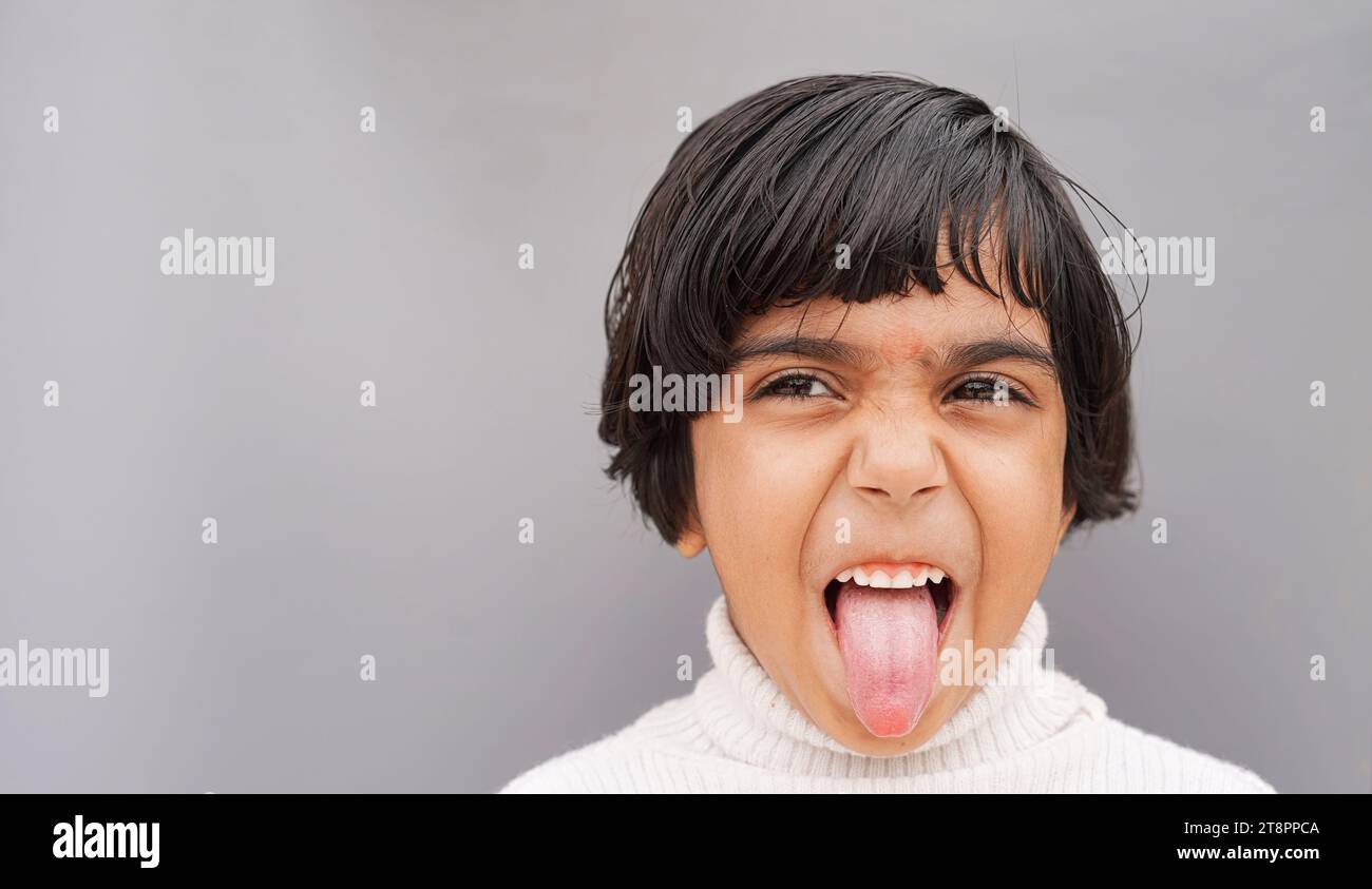 Primo piano con il ritratto della testa Happy Little adorabile asiatica ragazza dai capelli castani positiva che mostra la lingua, buffo grimace, prendere in giro, giocare, guardare la videocamera Foto Stock