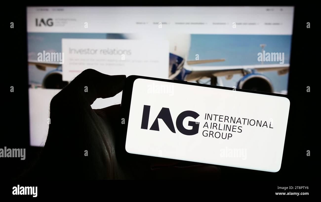 Persona in possesso di un cellulare con il logo di International Consolidated Airlines Group SA (IAG) davanti alla pagina Web aziendale. Concentrarsi sul display del telefono. Foto Stock