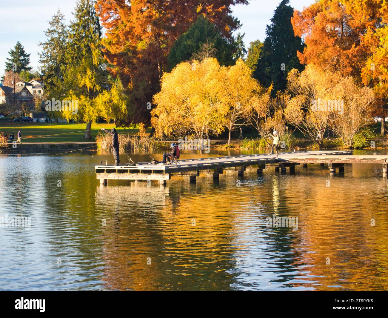 Figure sul molo del lago in lontananza nelle soleggiate giornate autunnali per praticare pesca sportiva e attività ricreative all'aperto al Green Lake Park di Seattle, Washington. Foto Stock