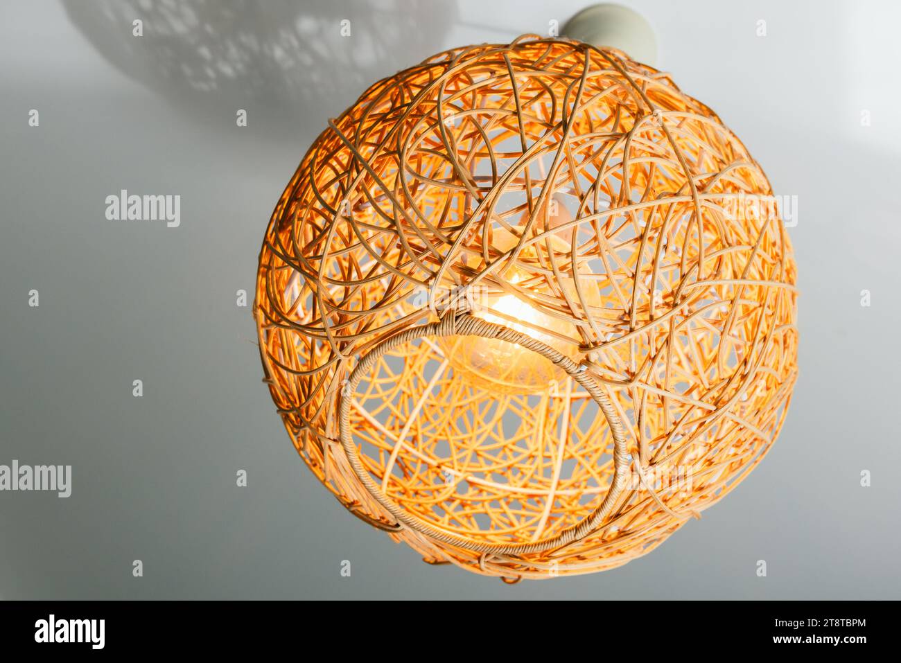 Lampadario moderno con paralume in paglia a forma di sfera appeso sotto il soffitto bianco, foto ravvicinate Foto Stock