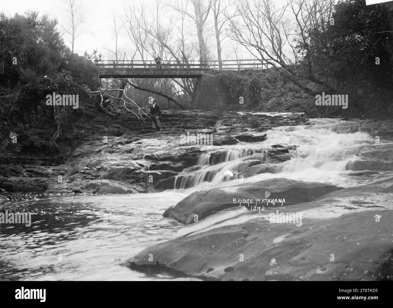 Il ponte e le cascate, Matakana, Vista delle cascate vicino al ponte di Matakana. Un uomo è in piedi sul ponte sullo sfondo e un altro è in piedi sulle rocce accanto alle cascate a media distanza. Fotografia scattata tra il 1910 e il 1930 Foto Stock Il ponte e le cascate, Matakana, Vista delle cascate vicino al ponte di Matakana. Un uomo è in piedi sul ponte sullo sfondo e un altro è in piedi sulle rocce accanto alle cascate a media distanza. Fotografia scattata tra il 1910 e il 1930 Foto Stock