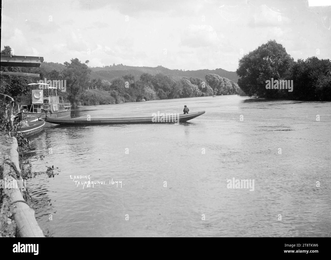 Uno sbarco sul fiume Whanganui a Taumarunui, veduta di uno sbarco sul fiume Whanganui a Taumarunui, con un battello a vapore lungo lo sbarco, e una canoa motorizzata che si estende nel fiume. tra 1900 e 1930 Foto Stock