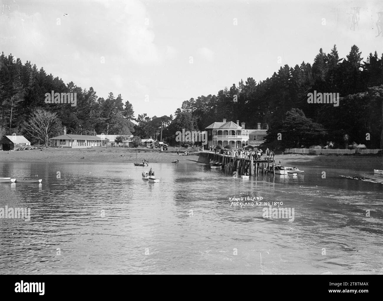 Mansion House, Kawau Island dall'acqua, Mansion House ed edifici vicini, Mansion House Bay, Kawau Island, presa dalla costa. Mansion House era probabilmente una guest House in quel momento. Un gruppo di persone sta aspettando il traghetto sul molo, all'inizio degli anni '1900 Foto Stock