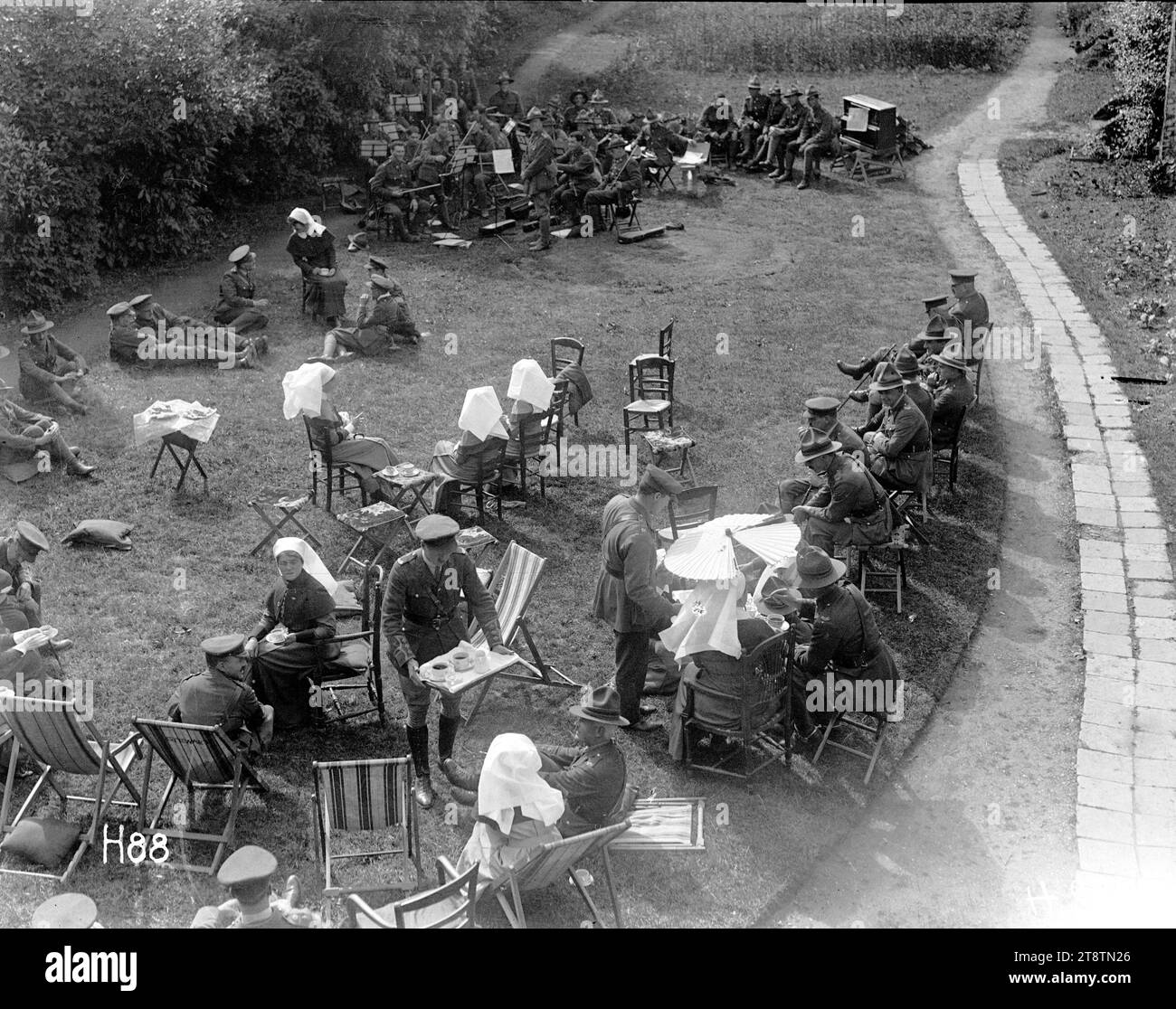 Infermieri del New Zealand Stationary Hospital dare una festa in giardino nel terreno, vista generale del giardino partito tenuto dalle infermiere della prima guerra mondiale presso il New Zealand Stationary Hospital, probabilmente a Hazebrouck, Francia. Gli ospiti si siedono sulle sedie o si sdraiano sull'erba. La Matron Frances Price siede, in basso a sinistra, parla con il generale Russell. Sullo sfondo un'orchestra dell'esercito ha smesso di suonare. Fotografia scattata il 24 giugno 1917 Foto Stock