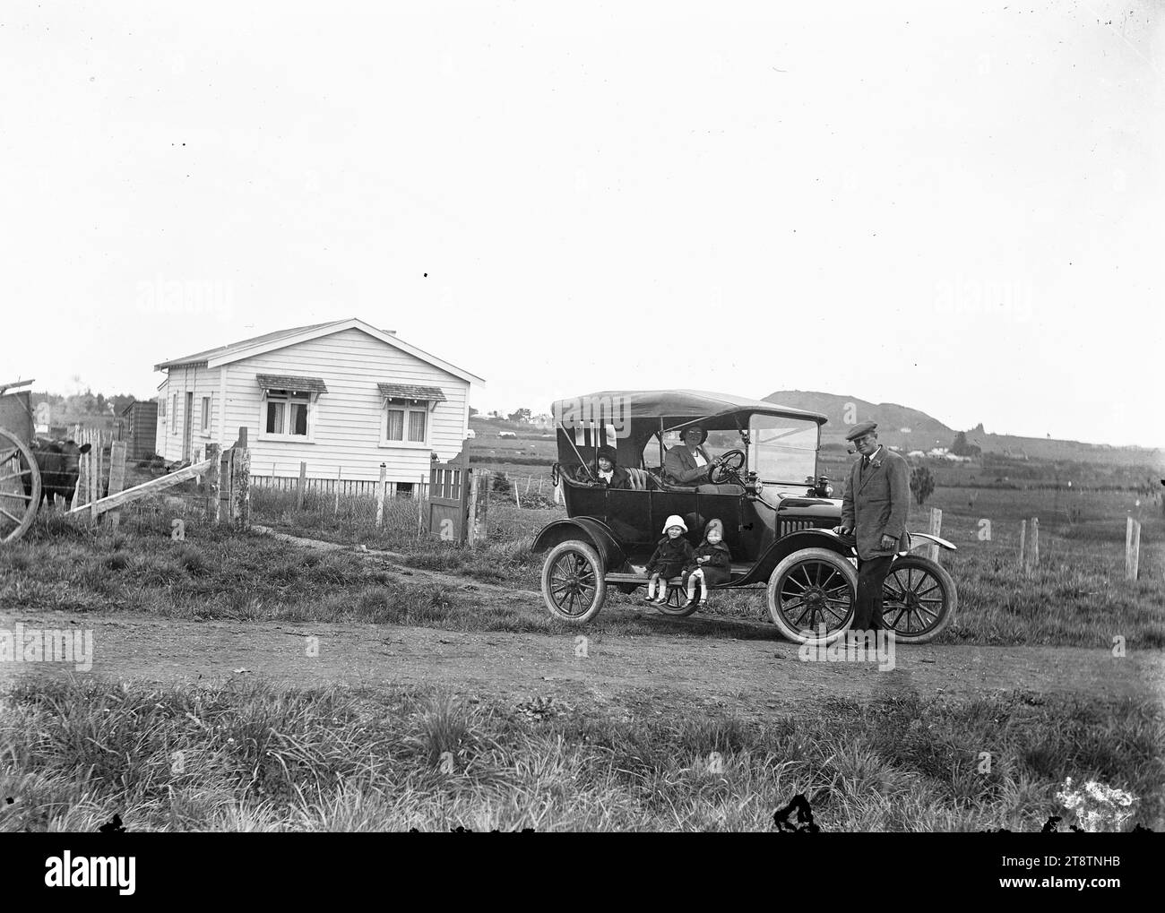 Model T Ford fuori da una fattoria, Una Model T Ford parcheggiata fuori da una fattoria. Una donna è al volante, un uomo in piedi vicino a una ruota anteriore, due bambini seduti sulle pedane, e un terzo sul sedile posteriore., CA 1920 Foto Stock