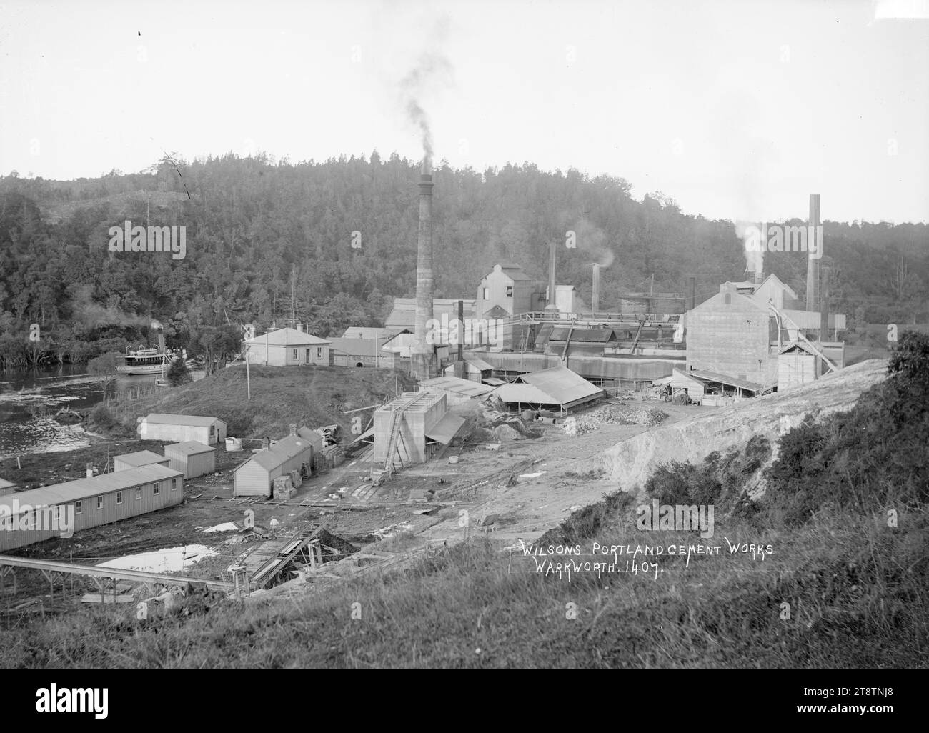 Wilson Portland Cement Works, Warkworth, Rodney County, mostra Portland Cement Works, Warkworth con il fumo che passa attraverso i camini. Un traghetto sul fiume Mahurangi può essere visto dietro i lavori sulla sinistra., CA 1910 Foto Stock