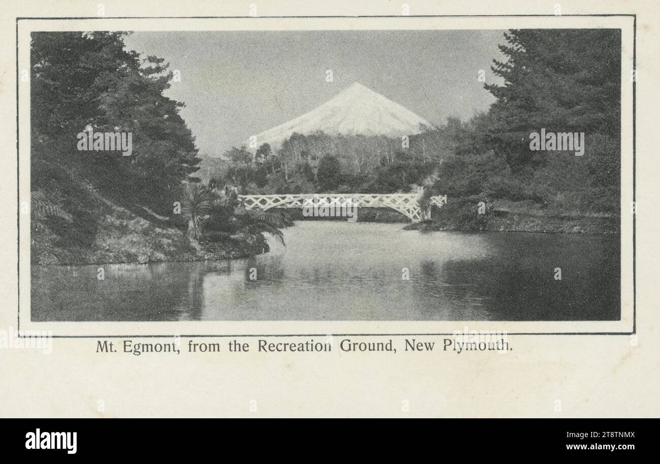 Cartolina. Monte Egmont, dal Recreation Ground, New Plymouth. 1900-1920, mostra un Monte Taranaki innevato visto da un lago o da un fiume, con un ponte dipinto di bianco in primo piano Foto Stock